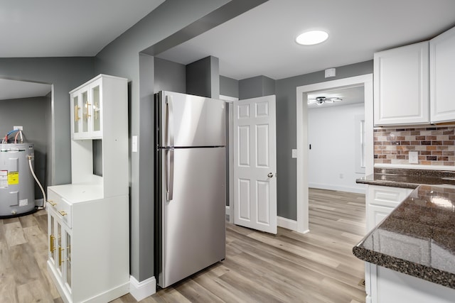  - kitchen with freestanding refrigerator, electric water heater, white cabinets, dark stone counters, and light wood-style floors