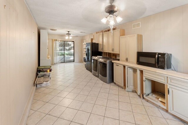 kitchen featuring ceiling fan, washer and dryer, wooden walls, light tile patterned floors, and black appliances