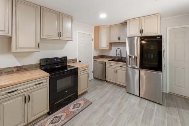 kitchen with wood counters, cream cabinets, stainless steel appliances, and sink