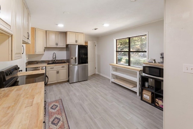 kitchen with stainless steel refrigerator with ice dispenser, light hardwood / wood-style floors, sink, cream cabinets, and butcher block countertops