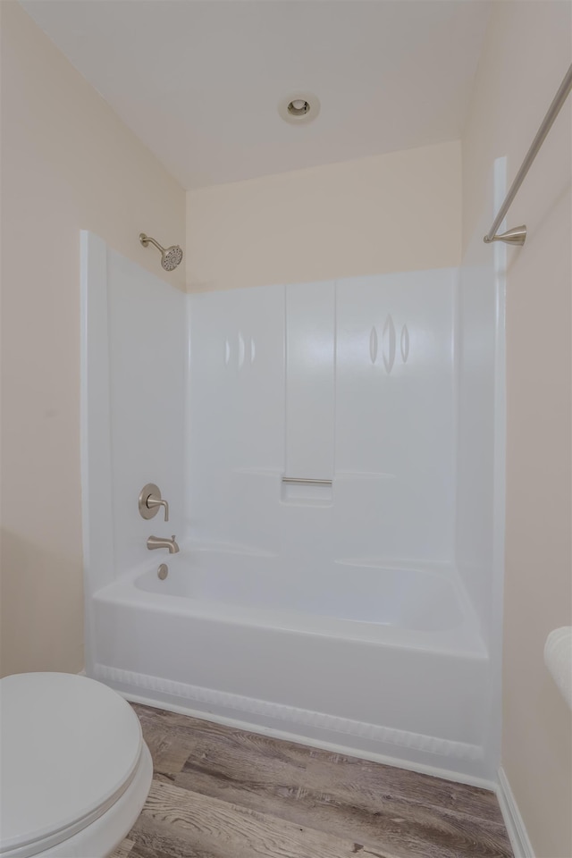 bathroom with hardwood / wood-style flooring, shower / washtub combination, and toilet