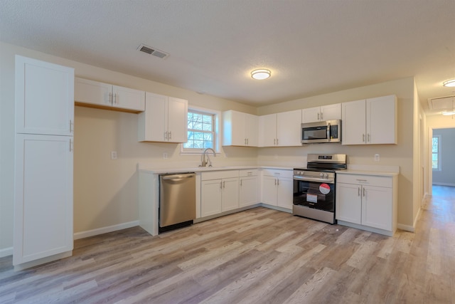 kitchen featuring sink, a textured ceiling, light wood-type flooring, stainless steel appliances, and white cabinets