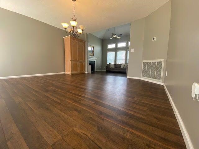  - unfurnished living room with dark wood-style flooring, a chandelier, baseboards, a ceiling fan, and a fireplace