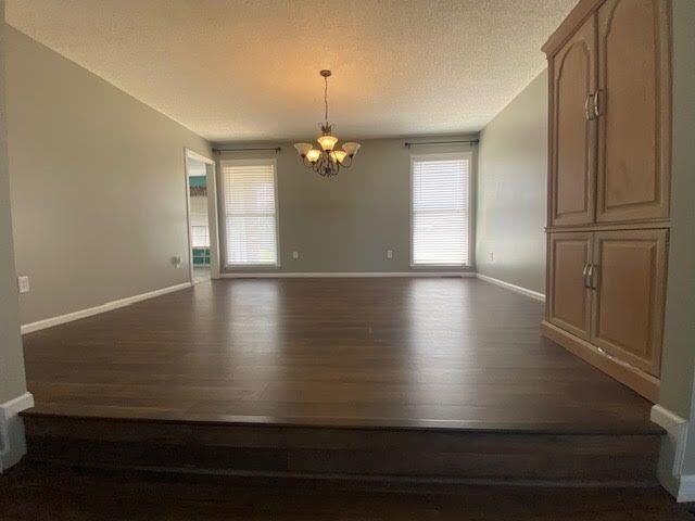  - unfurnished room featuring dark wood finished floors, a chandelier, a textured ceiling, and baseboards