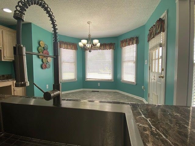  - kitchen featuring a chandelier, a textured ceiling, dark countertops, baseboards, and decorative light fixtures