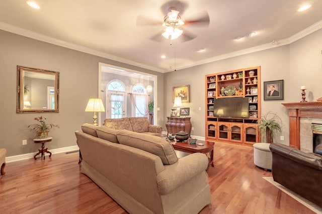 living room featuring light wood-type flooring, ceiling fan, crown molding, built in features, and a tiled fireplace