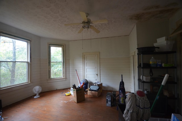 interior space with ceiling fan, wooden walls, a textured ceiling, and hardwood / wood-style flooring