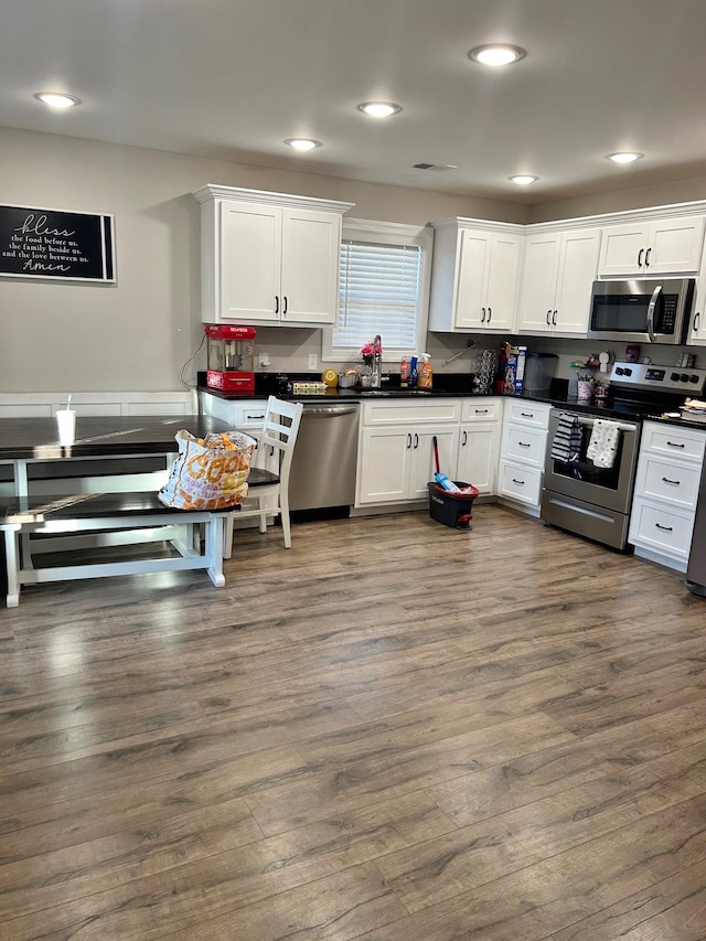 kitchen with appliances with stainless steel finishes, dark wood-style flooring, dark countertops, and white cabinetry