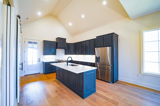 kitchen featuring premium range hood, high vaulted ceiling, a center island with sink, light wood-type flooring, and stainless steel appliances