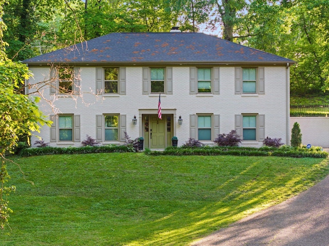 colonial inspired home with a front lawn, a chimney, and brick siding