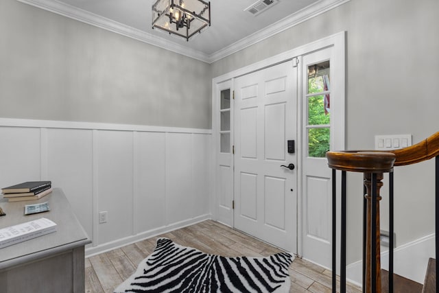 entrance foyer with a chandelier, crown molding, a decorative wall, light wood finished floors, and a wainscoted wall