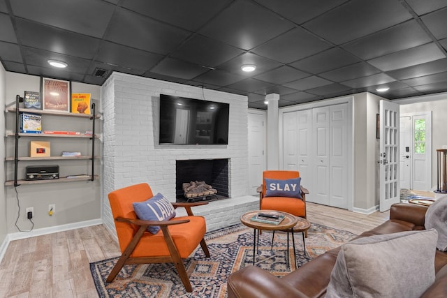 living room featuring wood finished floors, baseboards, a brick fireplace, and a paneled ceiling