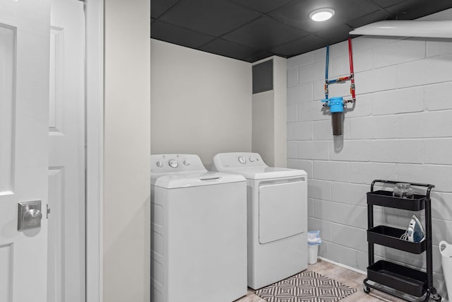 laundry area featuring concrete block wall, light wood-type flooring, and washing machine and clothes dryer
