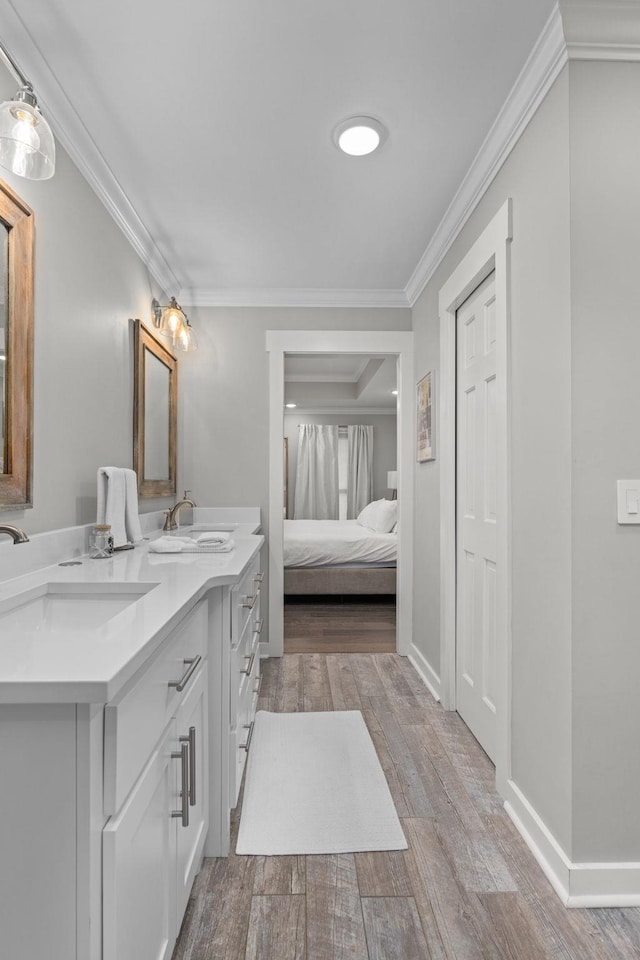 bathroom featuring wood finished floors, connected bathroom, double vanity, crown molding, and baseboards