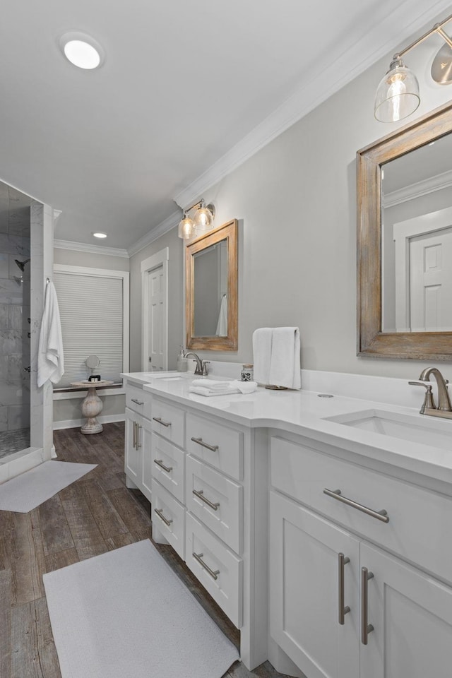 full bathroom featuring crown molding, double vanity, a shower stall, and wood finished floors