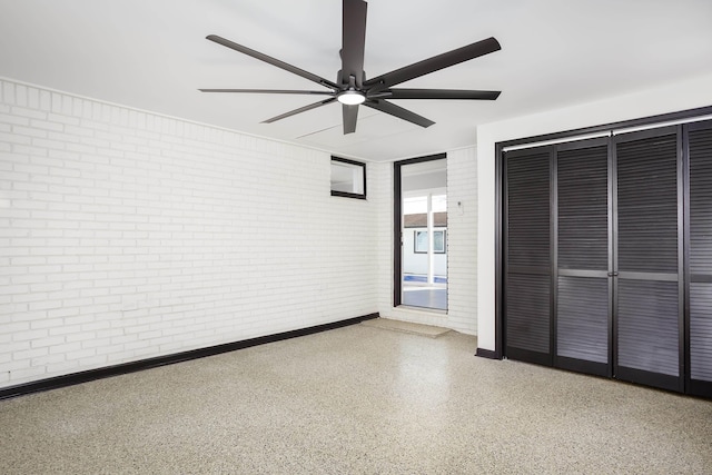 unfurnished bedroom featuring ceiling fan, brick wall, and a closet