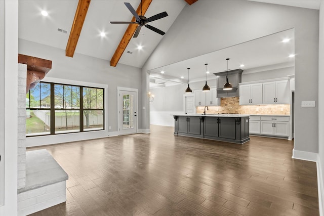 unfurnished living room with dark wood-type flooring, high vaulted ceiling, sink, ceiling fan, and beam ceiling