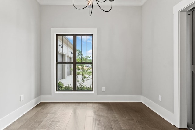 empty room featuring wood-type flooring, crown molding, and a chandelier