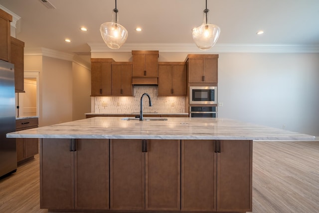 kitchen featuring a large island with sink, stainless steel appliances, sink, and decorative light fixtures