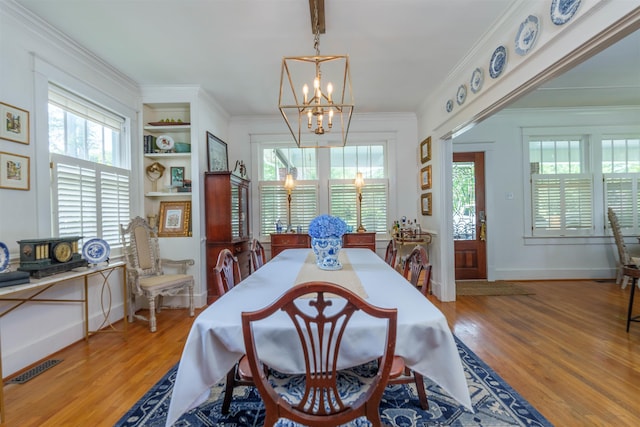  - dining space with a chandelier, plenty of natural light, wood finished floors, crown molding, and built in features