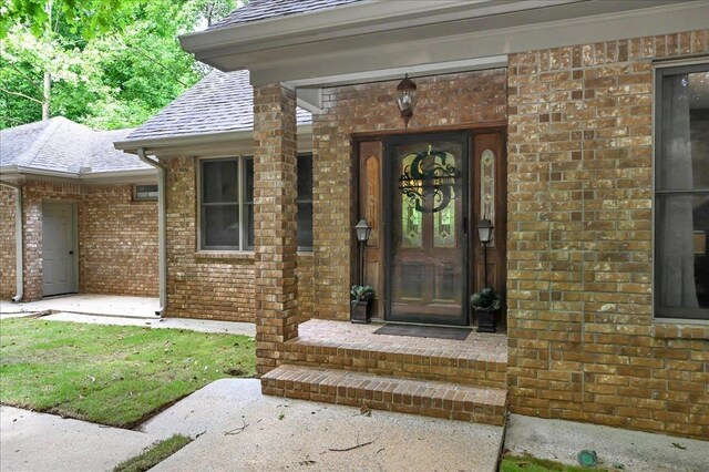  - doorway to property featuring brick siding and a shingled roof