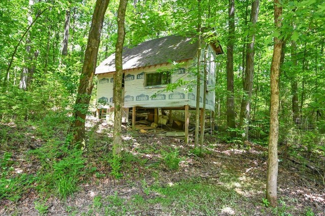  - rear view of property featuring a shingled roof and a wooded view