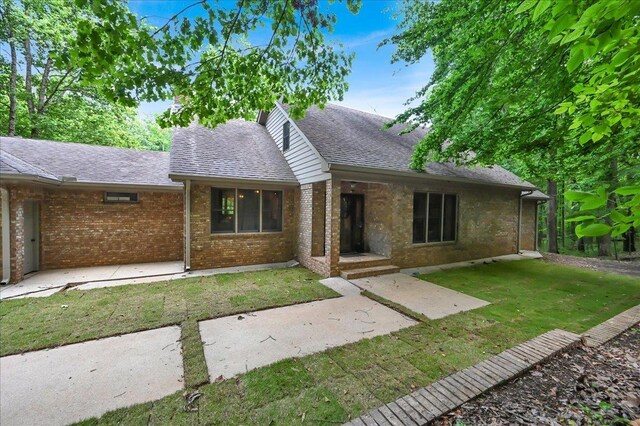  - view of front of home with a front yard, roof with shingles, and brick siding