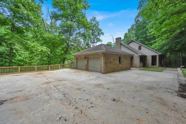  - view of property exterior featuring a chimney, an attached garage, brick siding, and concrete driveway