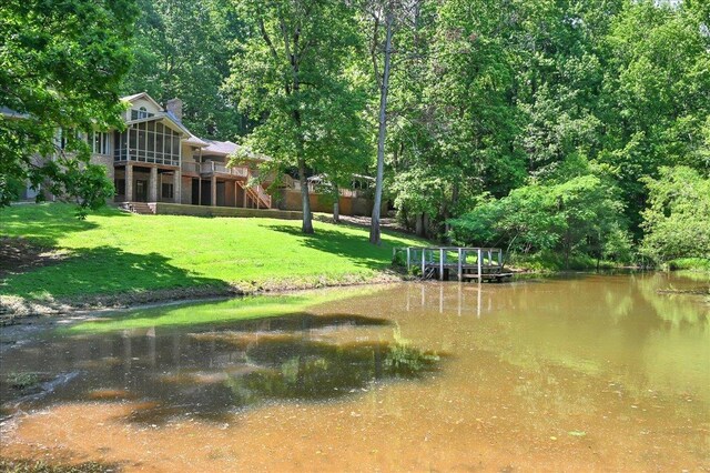  - view of green lawn featuring a forest view and a deck with water view