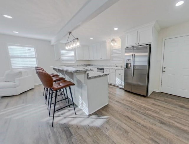 kitchen with decorative light fixtures, white cabinetry, a breakfast bar area, light stone counters, and stainless steel appliances