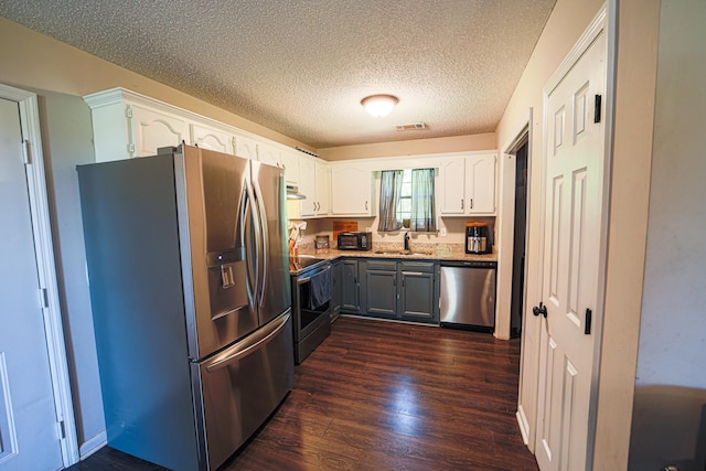 - kitchen featuring appliances with stainless steel finishes, a sink, dark wood-type flooring, white cabinetry, and a textured ceiling
