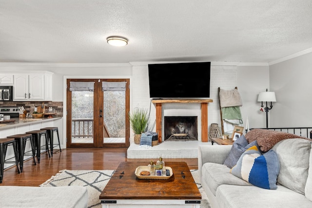 living room featuring dark wood-type flooring, ornamental molding, a textured ceiling, and a brick fireplace