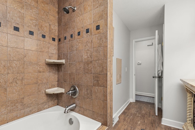 bathroom featuring a textured ceiling, wood-type flooring, and tiled shower / bath