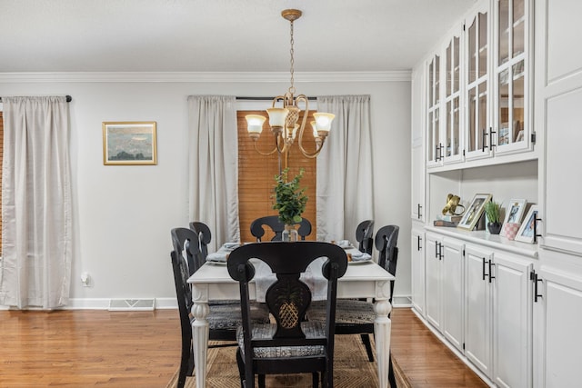 dining area with ornamental molding, wood-type flooring, and an inviting chandelier