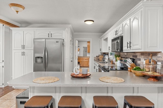 kitchen with a breakfast bar, white cabinets, ornamental molding, kitchen peninsula, and stainless steel appliances