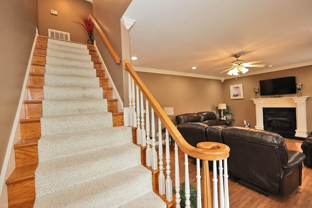 staircase with hardwood / wood-style floors, ceiling fan, and ornamental molding