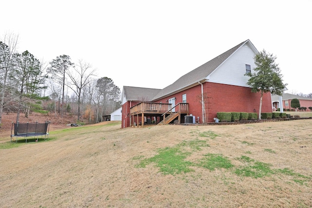 view of side of home with cooling unit, a trampoline, a lawn, and a wooden deck