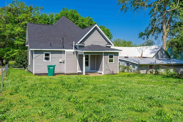 rear view of property with a lawn, roof with shingles, and fence
