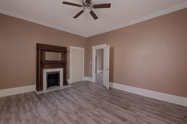 unfurnished living room with ornamental molding, wood finished floors, a fireplace, baseboards, and ceiling fan
