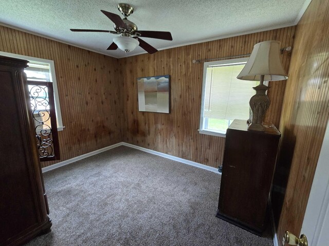  - empty room featuring a textured ceiling, crown molding, wood walls, carpet floors, and a ceiling fan