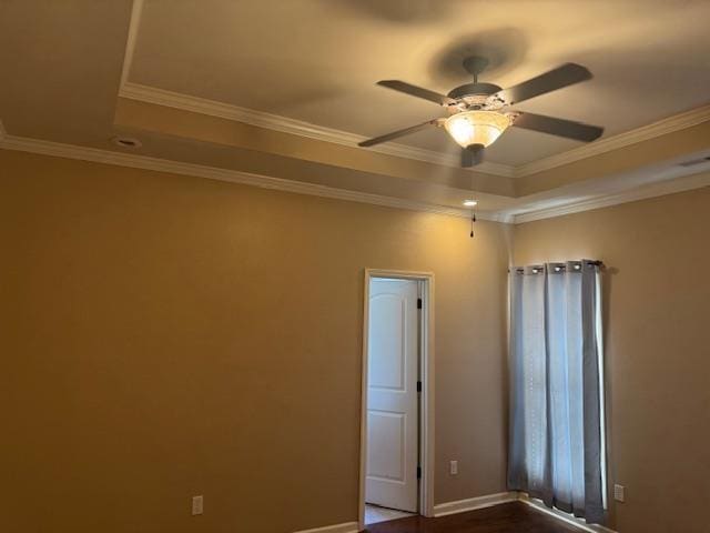 empty room featuring ceiling fan, baseboards, ornamental molding, and a raised ceiling