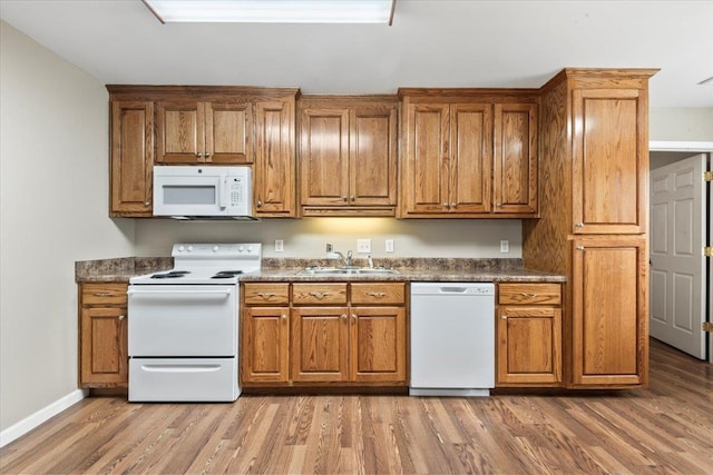 kitchen featuring white appliances, brown cabinetry, light wood-style flooring, and a sink