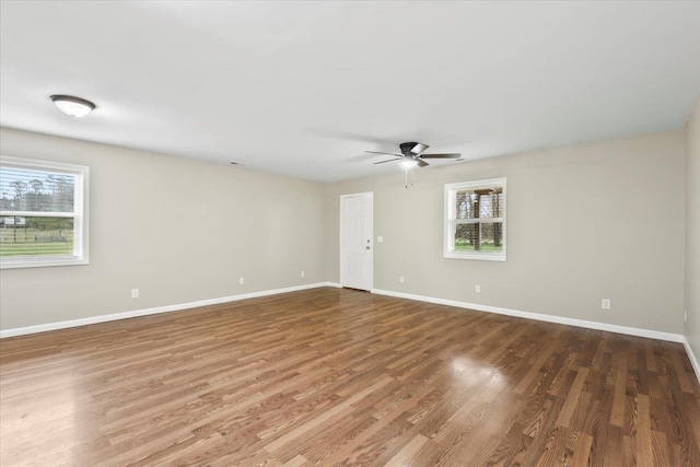 unfurnished room featuring baseboards, ceiling fan, wood finished floors, and a healthy amount of sunlight