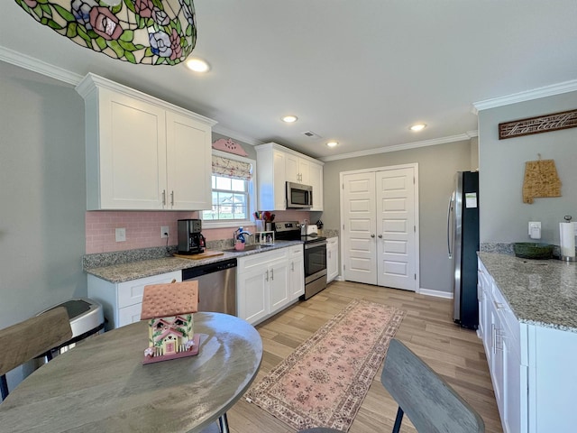 kitchen featuring light stone counters, crown molding, stainless steel appliances, white cabinets, and light wood-type flooring