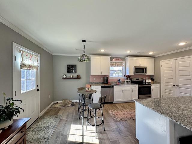 kitchen with light stone counters, white cabinets, ornamental molding, appliances with stainless steel finishes, and pendant lighting