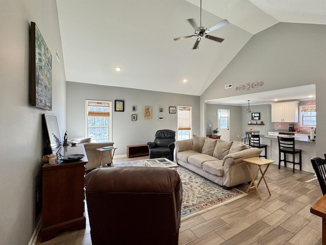 living room with visible vents, baseboards, light wood-style flooring, ceiling fan, and high vaulted ceiling