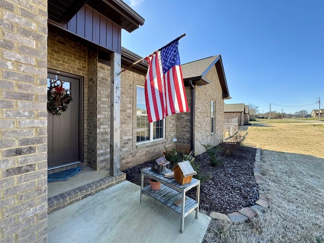 entrance to property with board and batten siding, brick siding, a yard, and a patio