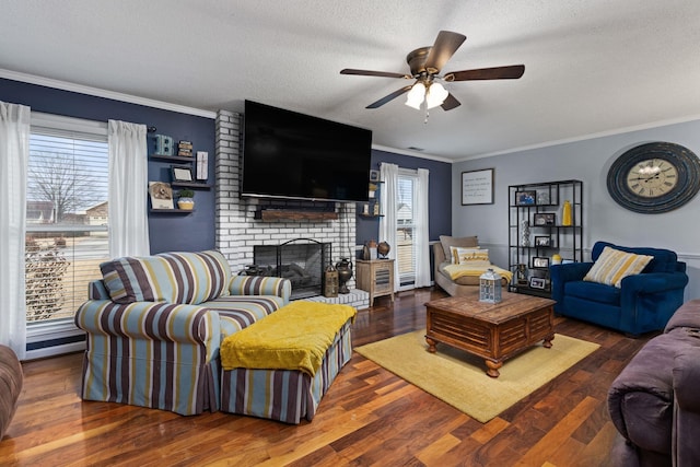 living area featuring a ceiling fan, wood finished floors, a textured ceiling, crown molding, and a fireplace