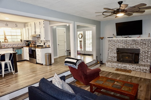 living room featuring french doors, light hardwood / wood-style floors, a wood stove, and sink