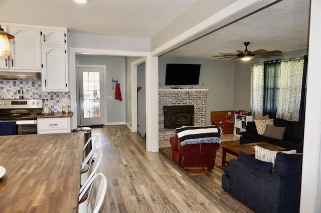 living room with light wood-type flooring, a wood stove, and ceiling fan